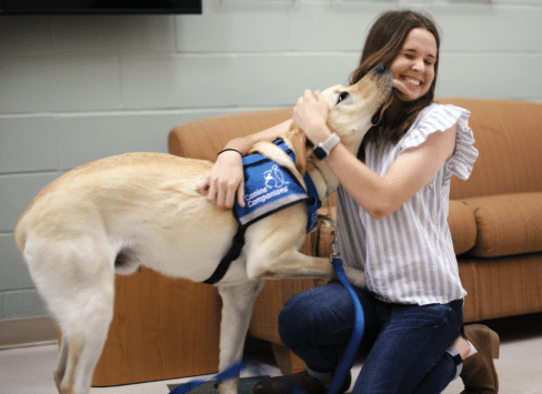 Girl happily hugging a service dog wearing a blue vest.